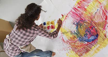 Video of biracial female artist painting on floor in studio