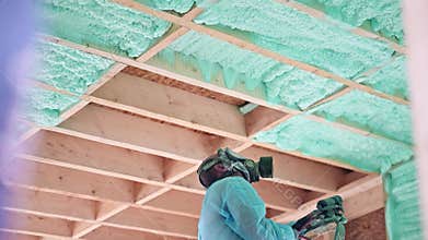 Worker spraying polyurethane foam for insulating wooden frame house.