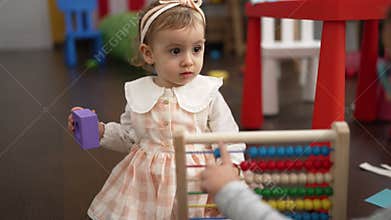 Adorable caucasian girl playing with abacus sitting on floor at kindergarten