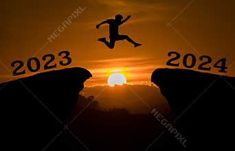 A young man jump between 2023 and 2024 years over the sun and through on the gap of hill silhouette evening colorful sky. happy ne