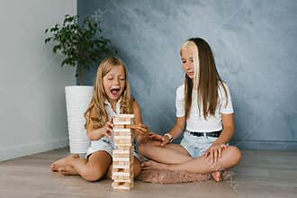 Sister girls are playing a board game of laying wooden blocks after school. Fun parties for kids, vacations at home
