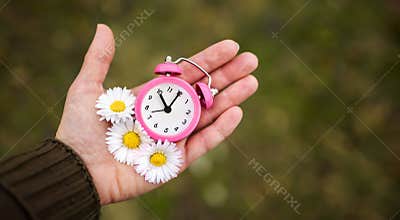 Alarm clock and flowers in a hand, daylight savings time or spring, summer banner