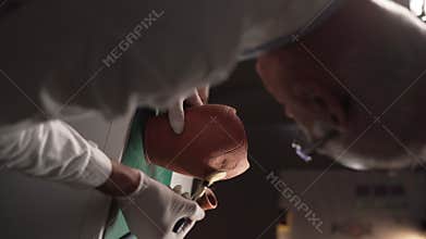 View over the shoulder of an old archaeologist working at night in a laboratory cleaning an artifact from contamination