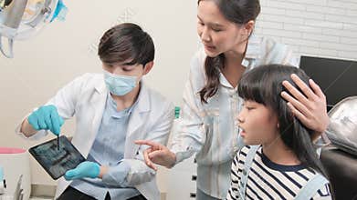 Asian male pediatric dentist explains teeth X-ray to a girl in a dental clinic.