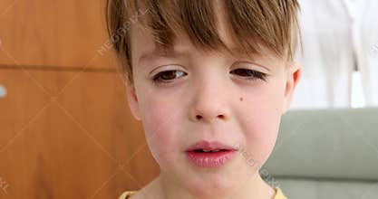 Little boy with long bangs looks down blinking in room