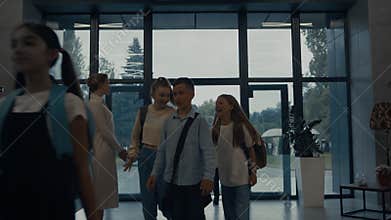 Group teen children entering in school building. Smiling teacher welcome pupils.