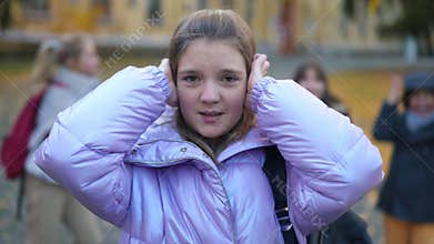 Stressed ashamed sad girl covering ears with hands looking at camera as blurred classmates making fun laughing at