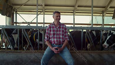 Happy farmer sitting cowshed feeder. Agro worker enjoying work process in barn.