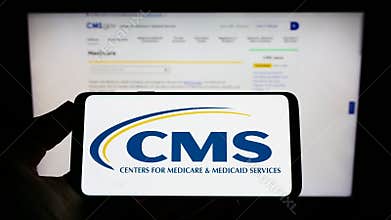 Person holding mobile phone with logo of Centers for Medicare and Medicaid Services (CMS) on screen with web page.