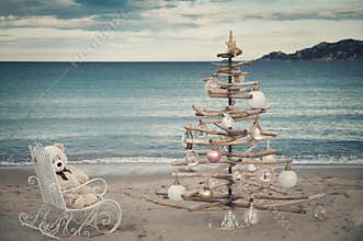 A Christmas tree a rocking chair with a Teddy bear   on the sandy beach