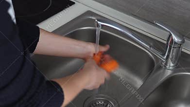 Woman washing carrots under water in the sink