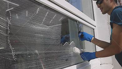 Professional male worker in overalls is engaged in cleaning and washing windows with special foam and tools in slow