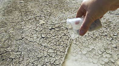 Hand pouring sand on dry, cracked earth