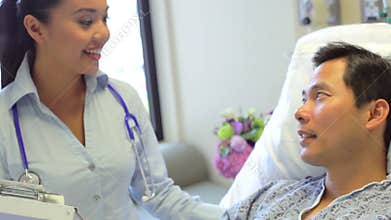 Female Consultant Talks To Male Patient In Hospital Room