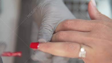 woman painting her nail with bright red gel polish on a manicure in a beauty salon