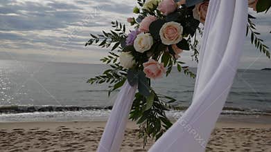 Romantic beach wedding arch with roses and flowing white fabrics near ocean, cinematic footage