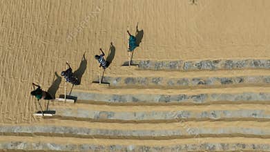 Aerial view of millions of grains of rice are laid out to dry at a mill as workers brush them with leaves in the hot sun.