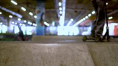Teenagers ride mini scooters in a skate park