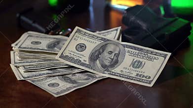 Film noir shot of 100 dollar bills falling in slow motion onto a gun.