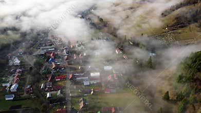 Rural village with misty forest, meadows and fields captured from above on a calm morning