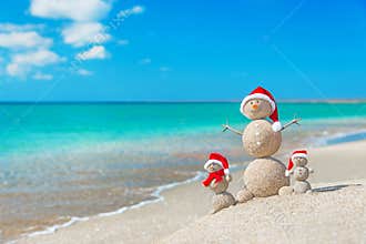 Snowmans family at sea beach in santa hat.