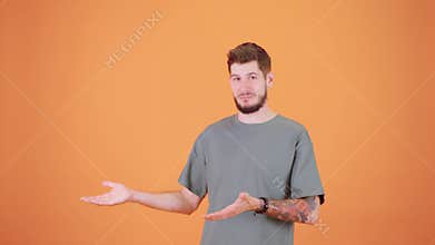A young man with a tattoo points to the side with a confident expression. He stands on an orange background, looking