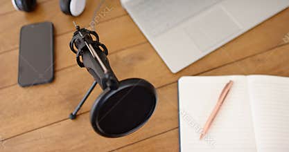 Podcasting setup with microphone, laptop, smartphone, and notepad on wooden table, at home