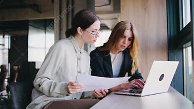 In a modern office, two ambitious women discuss using a laptop to enhance collaboration and idea sharing, aiming to
