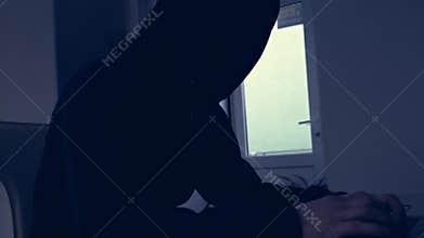Dark silhouette of a man in a hood, hacker, internet bandit, writing on a computer or laptop