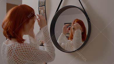 Redhead Woman Fixing her Hair in the Mirror
