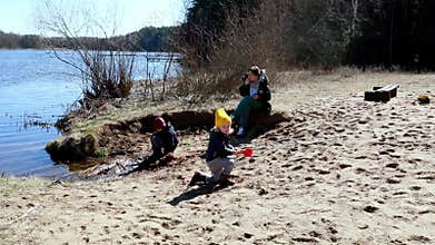Families enjoy a sunny day by the lake, kids playing in the sand and exploring nature together