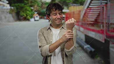 Hispanic man at construction site smiling while holding aching wrist in outdoor urban environment showing pain and injury