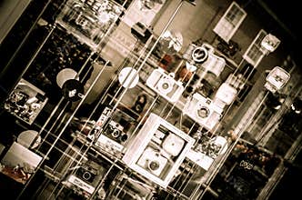 Various vintage cameras and photography equipment are arranged on glass shelves in a window display.