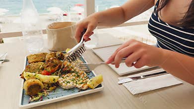 Woman Using Tongs To Grab And Serve Grilled Fish In Beach Restaurant