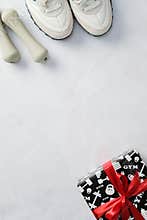 Fitness-themed flat lay with white sneakers, light green dumbbells, and a gift wrapped in black pape