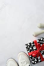 Flat lay with white sneakers, dumbbells, and gift box wrapped in red ribbon on marble background.