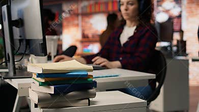 Stack of books on startup office desk in front of woman working, closeup