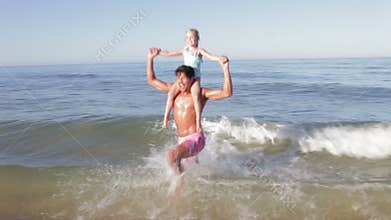 Father Carrying Daughter On Shoulders As They Run In Sea