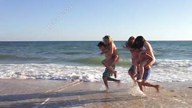 Teenage boys carrying girls along shore