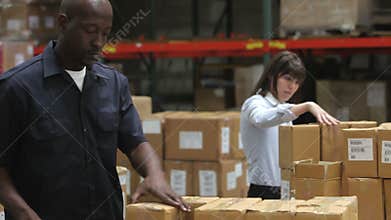 Worker Checks Clipboard As Colleague Seals Boxes