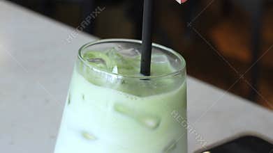 A close-up of a hand holding a black straw in a glass of iced green matcha latte