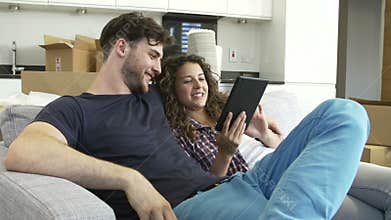 Couple Relaxing On Sofa With Digital Tablet In New Home