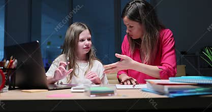 Mother sits at desk and explains math problem to daughter