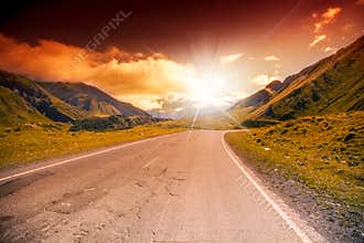 Road in the mountains landscape with bright sunset