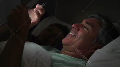 Middle Aged Couple In Bed With Man Using Tablet Computer