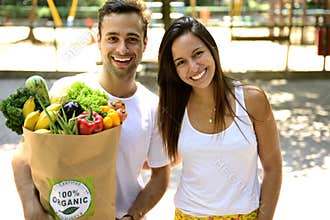 Happy couple carrying a recycle paper bag full of organic vegetables ans fruits.