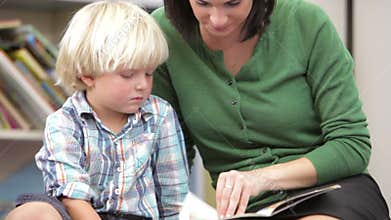 Teacher Reading Book With Male Pupil