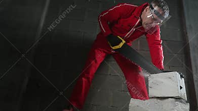 A man cuts bricks inside a building under construction.