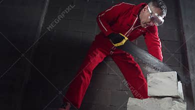A worker in overalls cuts bricks.