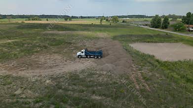 Blue truck on a barren patch of land under a cloudy sky, with houses and trees in the background